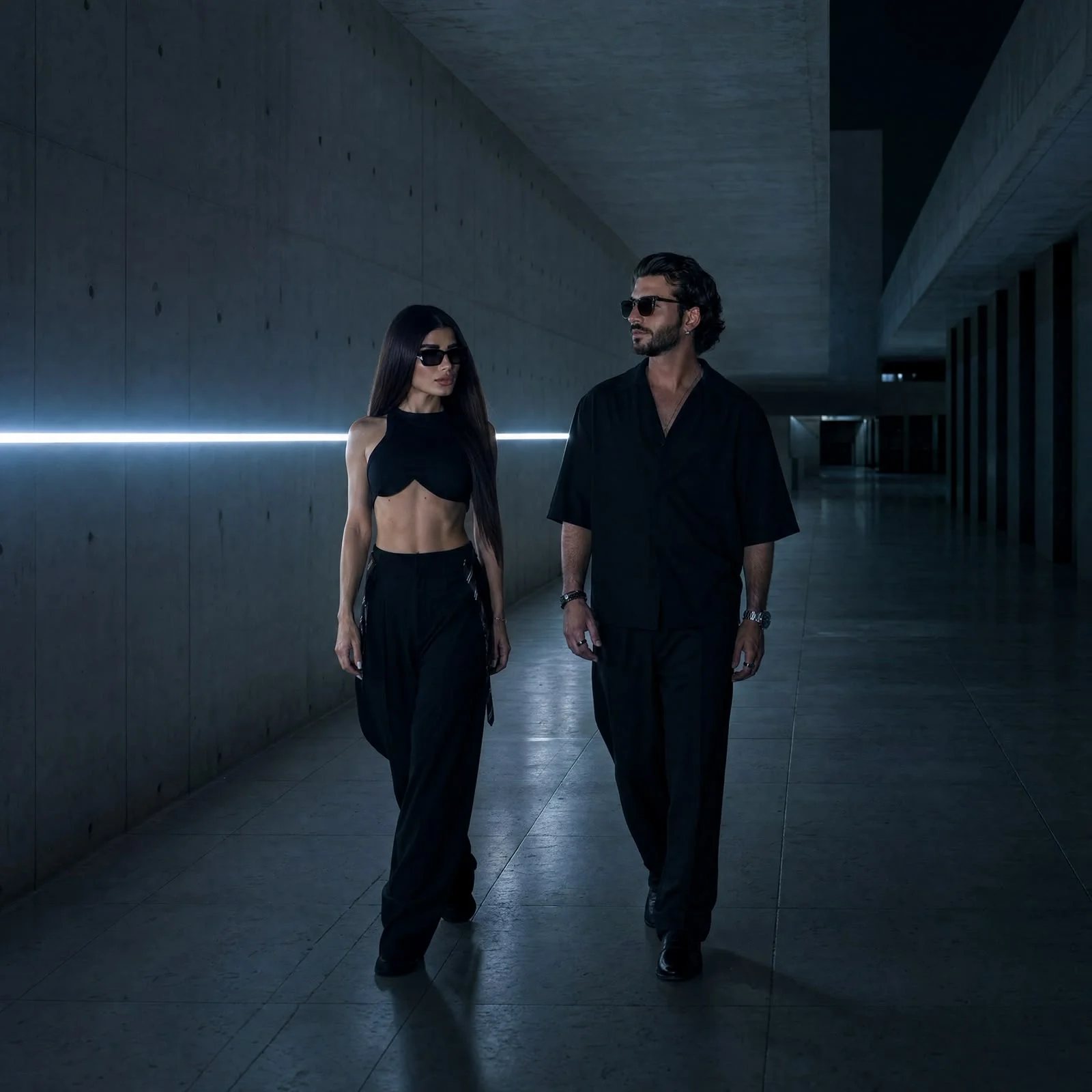 Deen and Noa walking through a concrete corridor lit by a single blue light strip